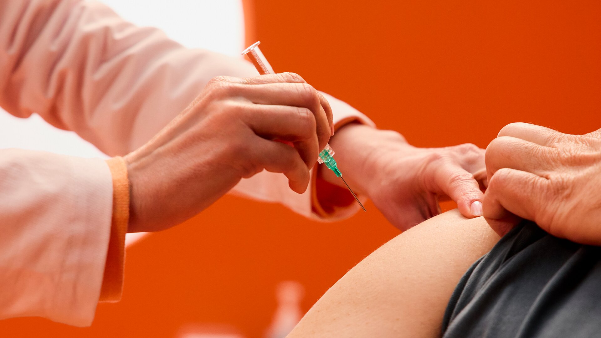 Apothekerin impft Patienten mit Spritze in den Oberarm in stilisiertem Impfzimmer.